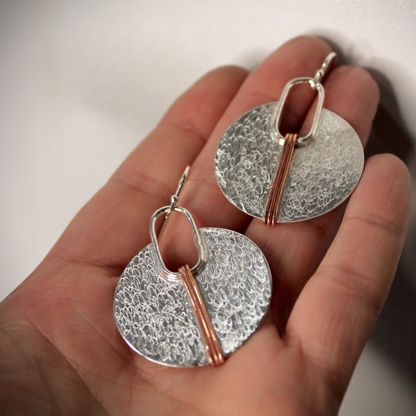 Silver circle with copper lines earrings shown on palm of hand