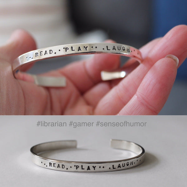 Message is Read Play Laugh with dots in between words stamped on silver bracelet. For a librarian who is also a gamer with a sense of humor